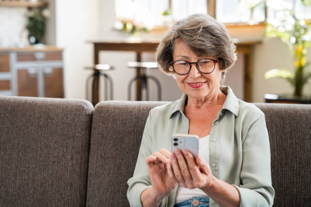 istock Cheerful caucasian senior woman using cellphone while relaxing on the sofa couch at home 2030600480