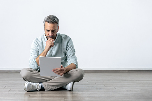 Caucasian man sitting on the floor and using digital tablet device. Studio shot.