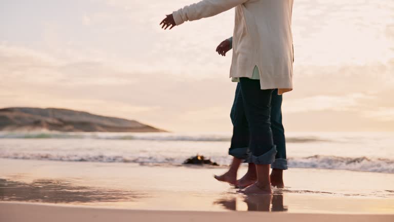 Couple, holding hands and walking on beach with legs, travel together with bonding, love and relax outdoor. People in nature, vacation with adventure and trust, marriage and support with commitment