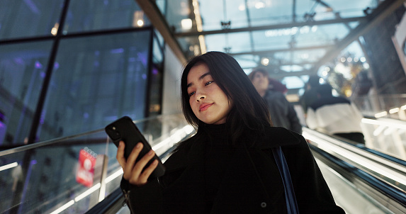 Japanese, woman on escalator and smartphone, travel and commute, communication with social media and adventure. Text, email and online chat with connectivity, mall or airport with mobile app in Japan