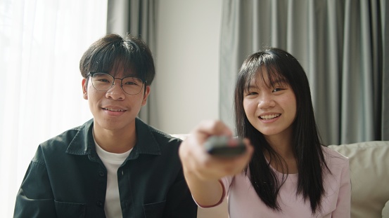 Two Asian teenager enjoy watching entertain channel on tv.