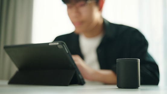 Young asian man sync bluetooth speaker with digital tablet.
