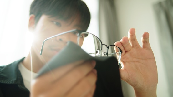 Asian teenage boy cleaning eyeglasses.