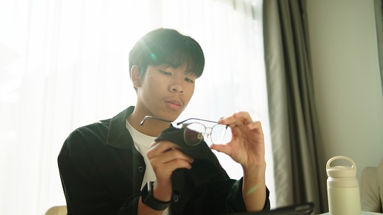 Asian teenage boy cleaning eyeglasses.