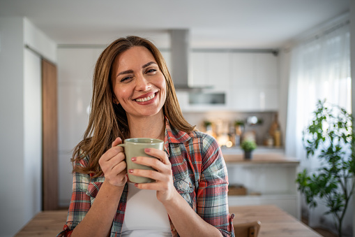 A young woman enjoys her morning coffee in her kitchen, dressed casually in a plaid shirt