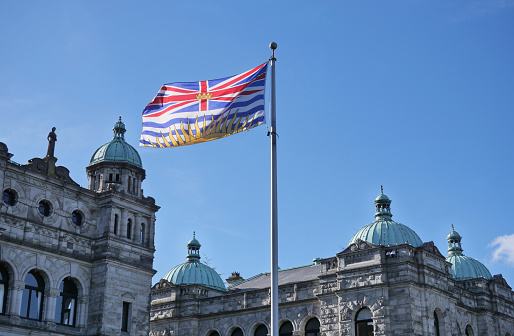Flag of British Columbia waving in front of the Legislative Assembly of British Columbia Parliament Building on Vancouver Island in Victoria, British Columbia, Canada.