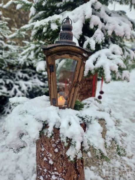 istock Decorated Christmas lantern with burning candle outdoors.Burning candle lantern with snow falling gently in the background. Branches fool will snow. 2030730391