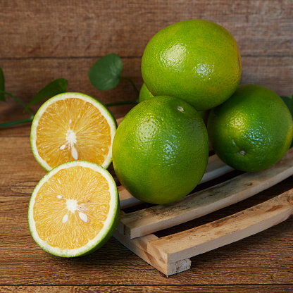 A fresh lime and orange halves on wooden tray with green leaves