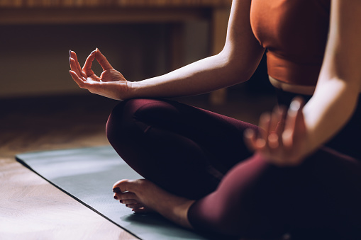 Close-up of a woman in a yoga pose, meditating with focus and tranquility on a mat in a dimly lit room.