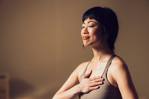 Peaceful mature woman with closed eyes practicing meditation. Feeling of tranquility, wellness, and self-care in a calm setting.