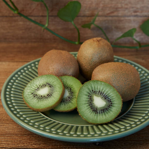 istock Whole and cut kiwis inside a green plate on a wooden background 2030734662