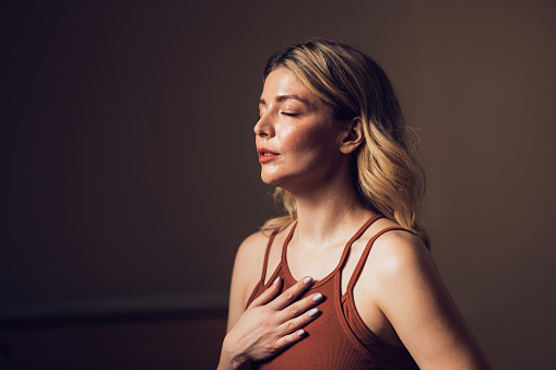 Portrait of a serene woman with closed eyes, hand on chest, engaging in a deep breathing exercise to find peace and mindfulness.