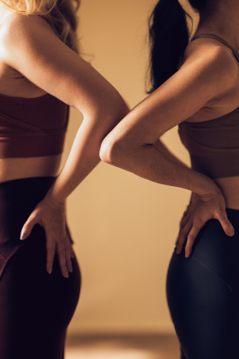Close up of two female fitness enthusiasts in sportswear performing partner yoga poses in a gym setting, showcasing wellness and teamwork.