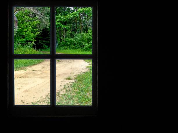 The photograph shows a landscape through a ruined window. The walls are damaged, bricks are visible. Outside the window, trees, a field, and a frozen pond are visible.