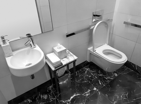 A modern bathroom with two sinks and a big mirror. The interior of the bathroom is modern and cosy. It's brown and beige. There are wooden details and bathroom cabinets and stone tiles. The bathroom is illuminated with beautiful led lights hidden behind the mirror and under the cabinets. There are some small candles to make the bathroom feel more homey.