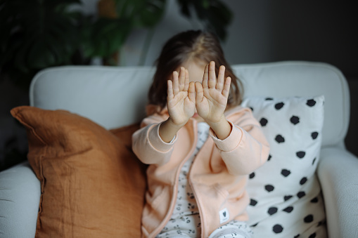 Sad child girl covers her face with her hand from violence