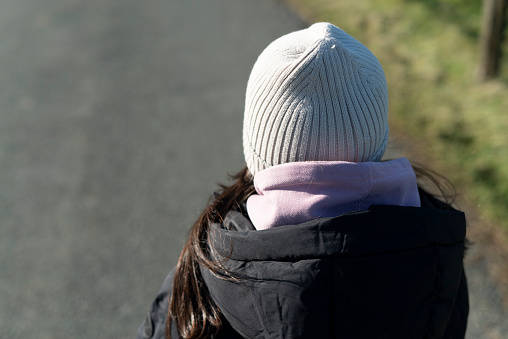 Back view of a young woman in winter jacket and hat on the road