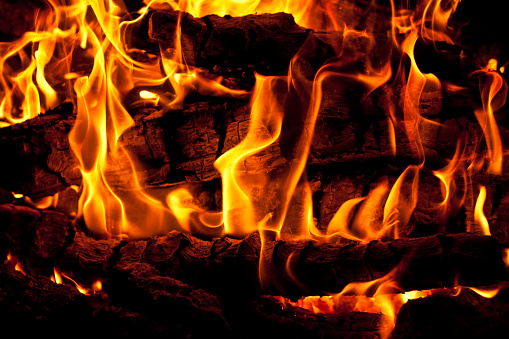Intense closeup of a roaring fire with high flames, radiating intense heat. The fire is fueled by wood, creating a mesmerizing display in a fireplace or campfire setting