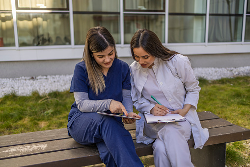 Nurses using digital tablet and working outdoor while sitting on the bench.