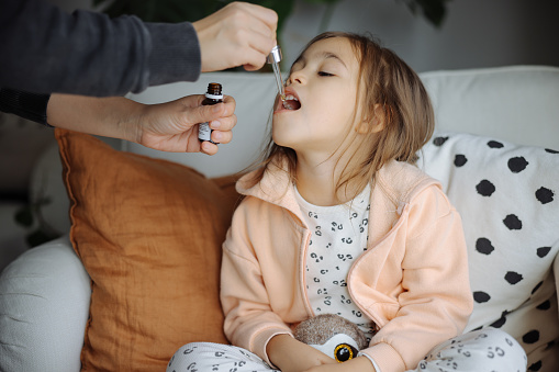 Sick girl taking a medicine from a spoon. Mother is taking care about her little girl