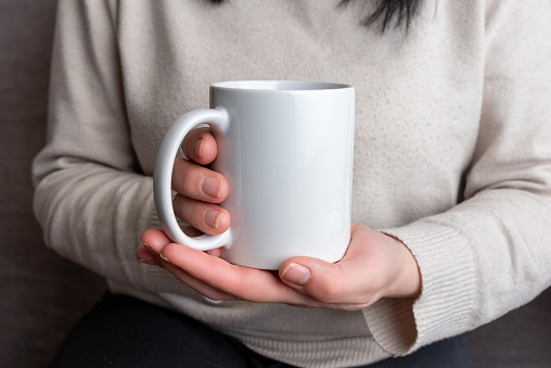 Woman's hands hold a pristine white mug, providing a perfect canvas for promoting mug designs