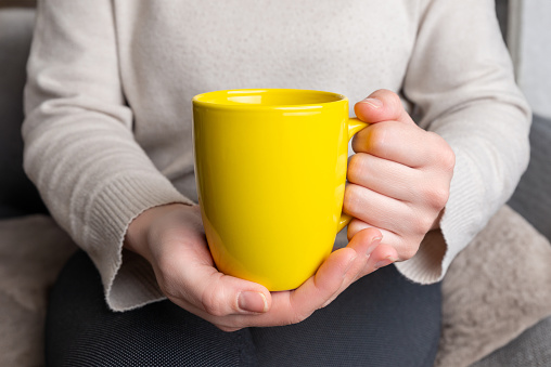 Woman's hands hold a yellow clean mug, providing a flawless surface for promoting custom mug designs