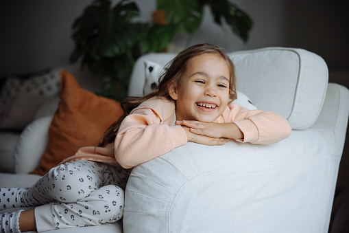 Carefree little kid girl sitting on sofa . Funny happy child playing and smiling. Family, vacation, childhood concept