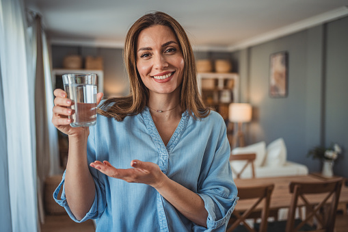 Portrait of a smiling young beautiful woman holding a glass of fresh clean drinking water. Concept of healthy lifestyle and fluid intake