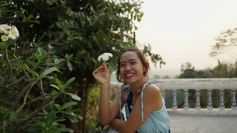 Thai woman picks a flower and smiles at the camera