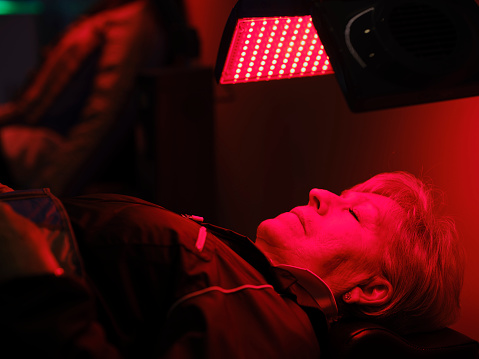 A senior aged woman on a bed, receiving LED red light therapy.