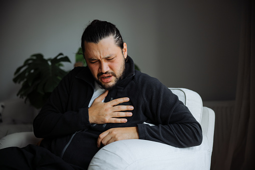 Asian woman standing against window with hand touching her chest in morning having heart attack