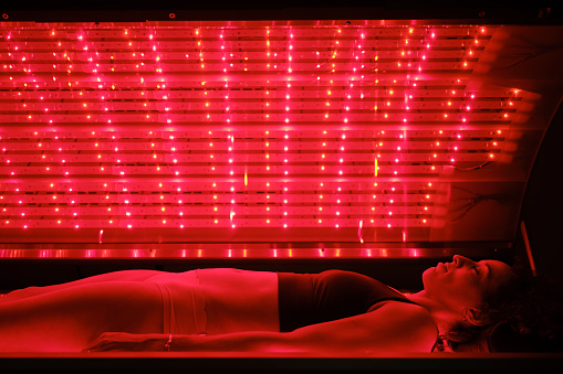 A multiracial woman on an LED light bed, receiving red light therapy.