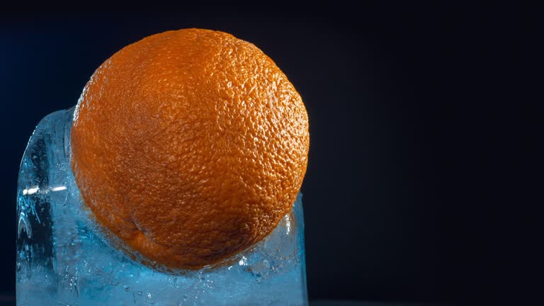 Frozen orange inside a block of ice with blue light melting against dark background