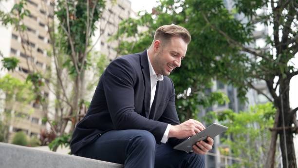 istock Businessman sitting at park while working on tablet by reading report. Urbane 2031070612