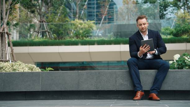 istock Businessman sitting at park while working on tablet by reading report. Urbane 2031071641