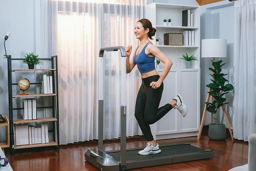 Energetic and strong athletic asian woman running running machine at home. Pursuit of fit physique and commitment to healthy lifestyle with home workout and training. Vigorous