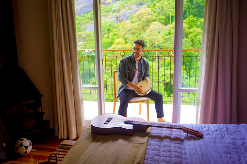 man is singing and playing tambourine on hotel room balcony. In the foreground details of the room