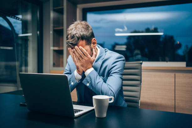 Businessman working late in the office. Shot of stressed businessman working with laptop at office during night. Exhausted businessman having a headache in modern office. Tired man working late in his office. Overworked businessman staying late hours in the office and using laptop. tired after work stock pictures, royalty-free photos & images