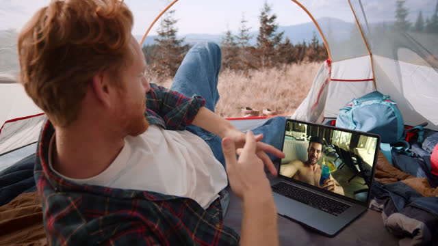 Two men talking video conference with laptop closeup. Traveling guy resting tent
