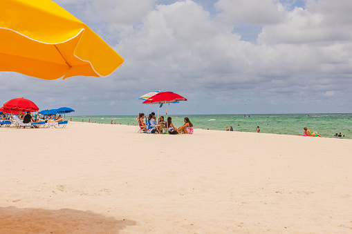 Miami Beach. USA. 02.22.2024. Group of friends under sun umbrellas on the shores of Miami Beach.