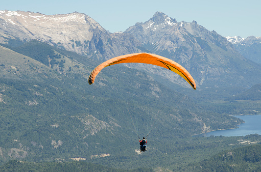 paraglider, instructor and passenger flying over lakes and mountains of bariloche, doing extreme sports at high altitude