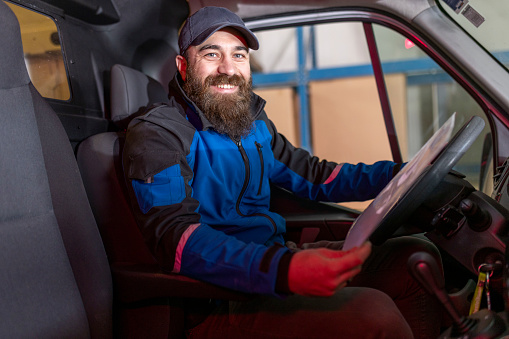 Portrait of a smiling delivery man sitting in a delivery van holding a list of merchandise to be unloaded