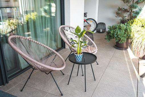 Elegant and comfortable outdoor seating area with stylish rattan chairs, a central table with a potted plant, all set on a sleek tiled patio. This serene space in a contemporary home invites relaxation and leisure time.