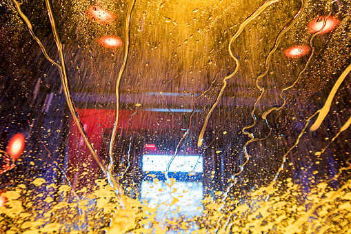 Automatic car wash customer driver's partially obscured view looking ahead through splattered falling car wax solution and pressure sprayed rinsing water draining in winding rivulets down the windshield glass.