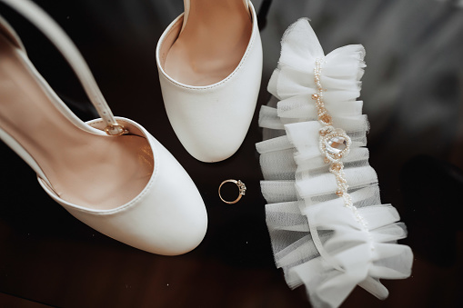 White elegant shoes. A pair of classic white shoes, a white beaded bridal headband and a wedding ring on a black background. Fashion. Style. Wedding photo