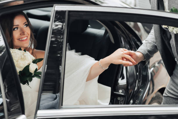 istock A brunette bride, smiling sincerely, sits in a black car on her wedding day and shakes hands with the groom, looking at him. Portrait of the bride. Beautiful makeup and hair. A luxurious white dress 2031568521