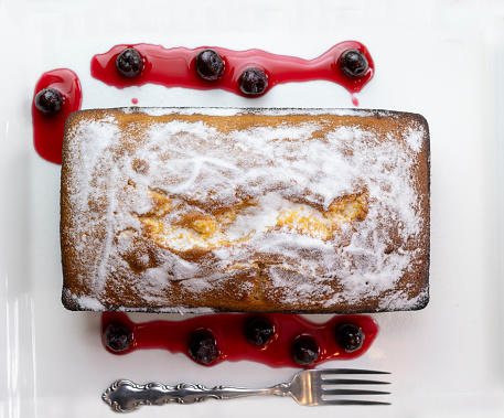 Golden citric sugar coverend pound cake loaf with cherries in a their syrup on a white ceramic plate