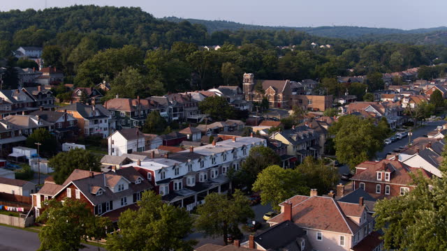 Row houses and a church surrounded by a tree area in Palmerton, PA during the summer. Holy Trinity Lutheran Church towers the cityscape. Aerial footage with panning-forward camera motion