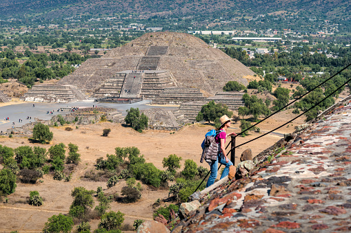 Tourist climbs the Pyramid of the Sun at the Teotihuacan pyramids, near Mexico City, Mexico on a sunny day, with the Pyramid of the Moon in the background.
