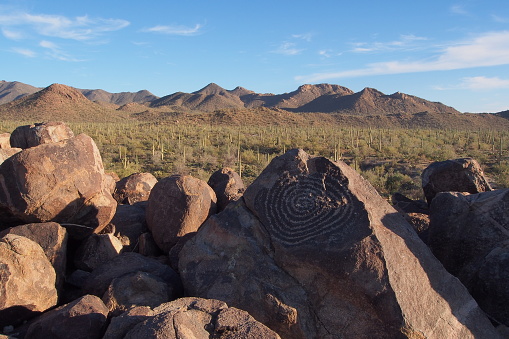Spiral petroglyph attributed to Hohokam people on Signal Hill in Saguaro National Park, Arizona, with mountains and saguaro cacti in the background.